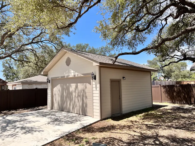 Tan single-bay garage tucked under oak trees